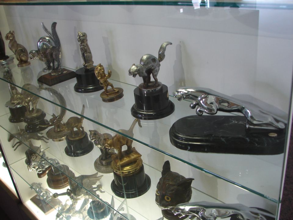 Display case with various car hood ornaments, including several jaguar figures and cat figures