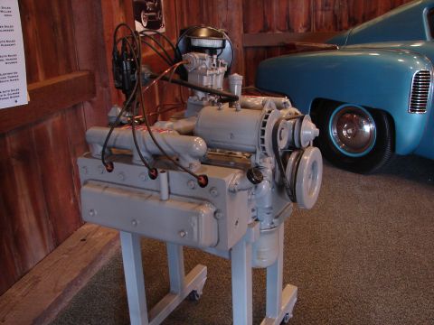 1993 Ford Taurus - A gray engine is displayed on a stand, with a portion of a blue vintage car visible behind it.