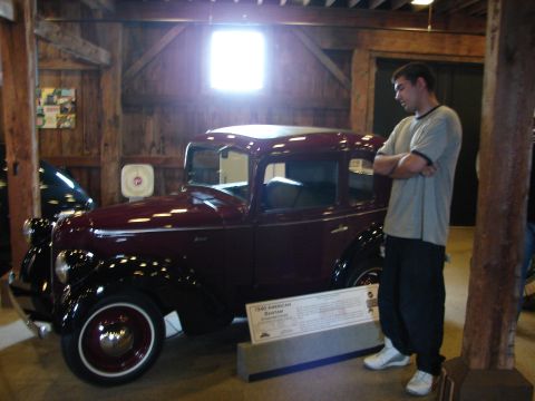 1993 Ford Taurus - A man stands next to a maroon 1939 American Bantam sedan on display in a barn-like structure.