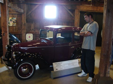 1993 Ford Taurus - A maroon 1940 American Bantam sedan is displayed indoors with a man observing it.
