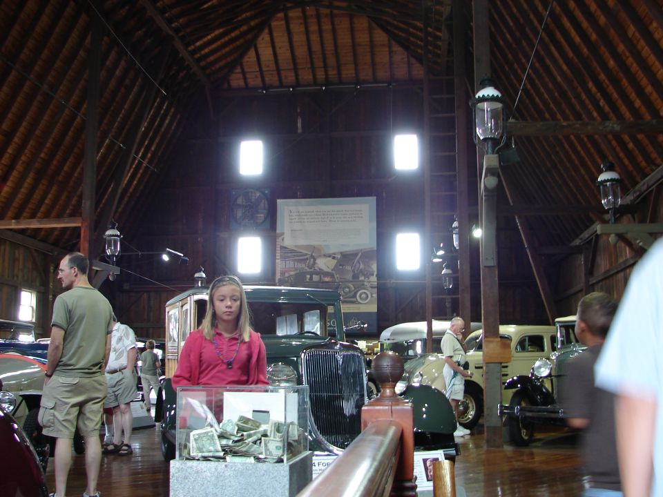 Barn interior with multiple vintage cars, a young girl in pink, and several adults