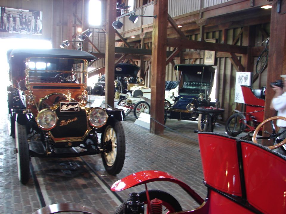 Several antique automobiles displayed indoors, with a black and gold car in the foreground