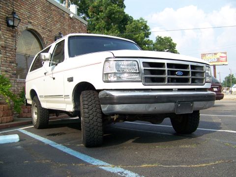 1995 Ford Bronco - A white Ford Bronco is parked in a lot, showing its front grille and tires.