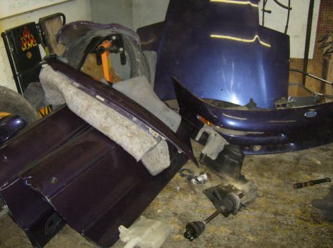 1996 Ford Probe - Disassembled car parts, including a hood and bumper, are scattered on a workshop floor.