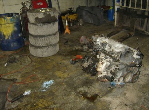 1996 Ford Probe - Engine assembly sits on a dirty garage floor next to a stack of tires and various tools.