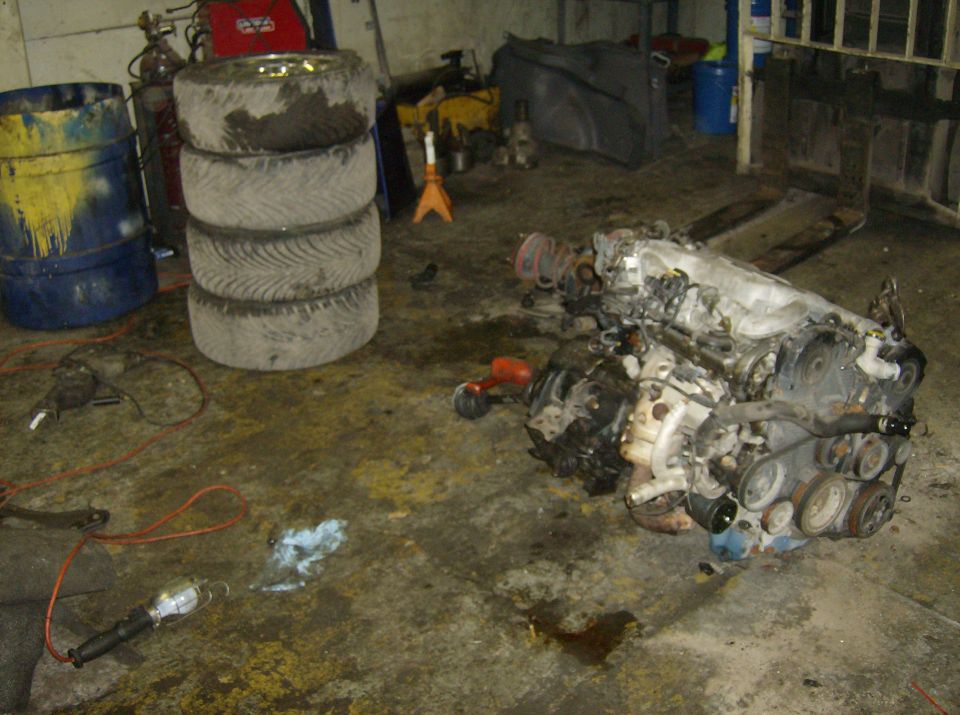 Engine assembly on a garage floor with stacked tires and tools