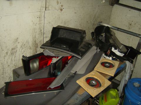 1996 Ford Probe - Various car parts, such as tail lights and speakers, are stored together in a cluttered space.