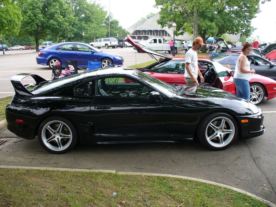 Black sports car with a large rear spoiler, side view. Aftermarket wheels are visible