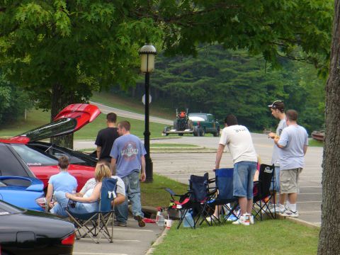 1991 Ford Probe - Several people are gathered around a red car with its trunk open in a parking lot with other vehicles.