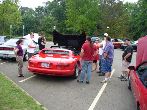 1991 Ford Probe - A group of people examine a red sports car with its hood open in a parking lot.