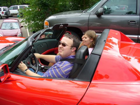 1991 Ford Probe - A red convertible sports car is driven by a man with a woman as a passenger, with other vehicles in the background.