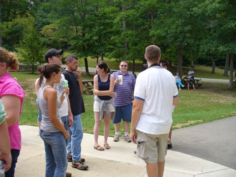 1991 Ford Probe - A group of people are seen socializing in a park, with trees and picnic tables in the background.