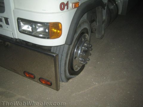 1990 Ford Bronco - front corner of a white commercial truck at night, showing a headlight, amber signal, chrome bumper with red markers and a front wheel.