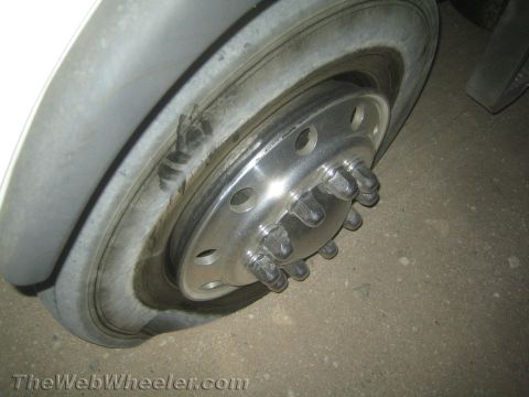 1990 Ford Bronco - close-up of a commercial truck's steel wheel and hub, showing the lug nuts and wheel studs, on a dusty surface.
