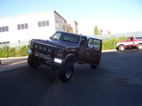 1991 Ford Bronco - Lifted maroon Ford Bronco with its door open, parked next to another Bronco.