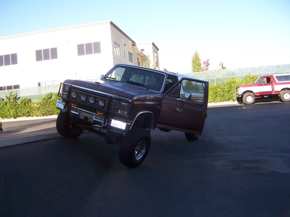 Lifted maroon Ford Bronco with door open, front grille with four lights