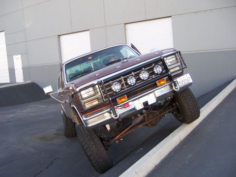 1991 Ford Bronco - This lifted Ford truck, likely from the early 1980s, is parked at an angle on a curb in front of a modern building.