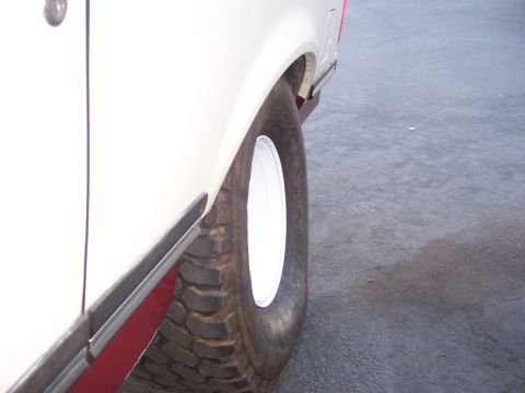 1991 Ford Bronco - Close-up of a large tire and fender on a white vehicle parked on asphalt.