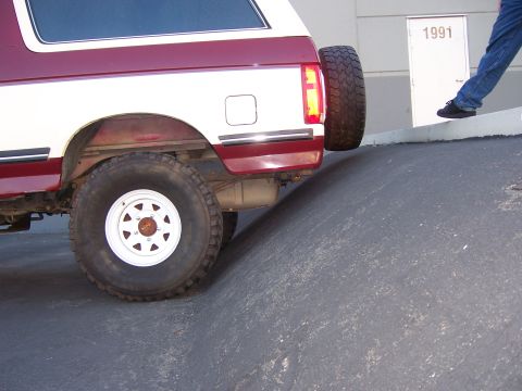 1991 Ford Bronco - Rear view of a two-tone 1991 Ford Bronco on a ramp, with a door labeled '1991' in the background.