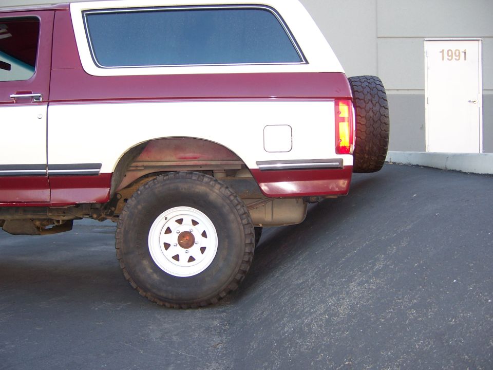 Rear quarter view of a two-tone red and white Ford Bronco parked on a ramp next to a door labeled 1991
