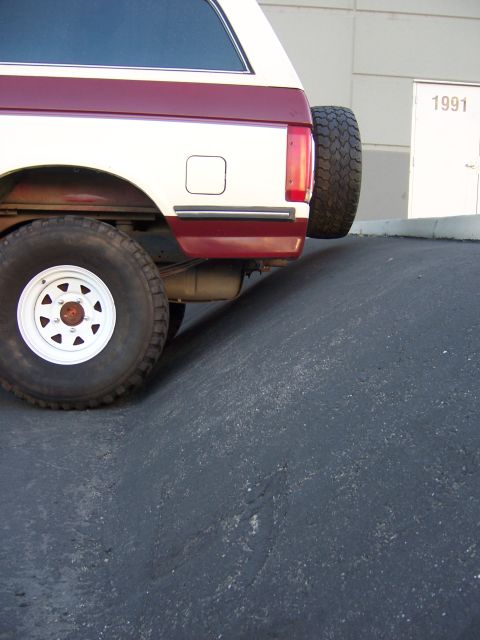 1991 Ford Bronco - The rear of a 1991 Ford Bronco is visible, parked on an incline in front of a building with the number 1991 on the door.