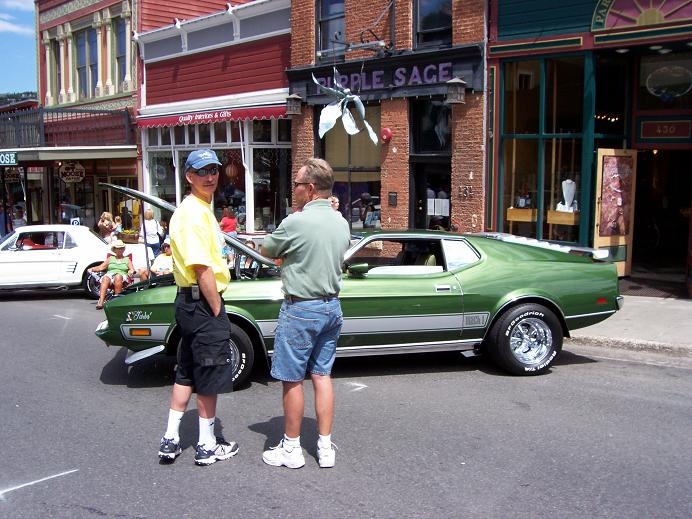 Green muscle car with two guys standing next to it. White car in background