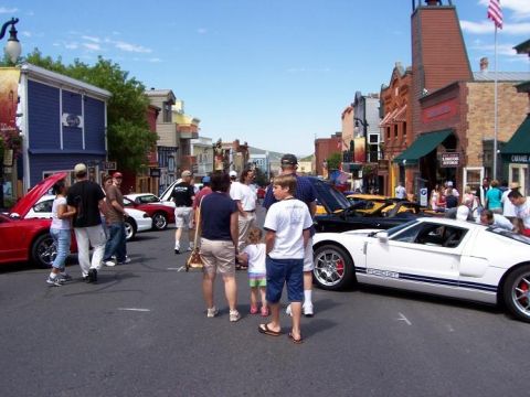 1972 Ford Ranchero - A white Ford GT with blue racing stripes is displayed on a street alongside other vehicles and pedestrians.