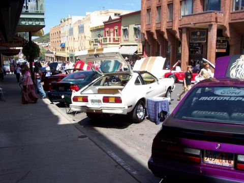 1972 Ford Ranchero - Several cars are parked along a street with buildings in the background. The white car has gold stripes on its hood and trunk.