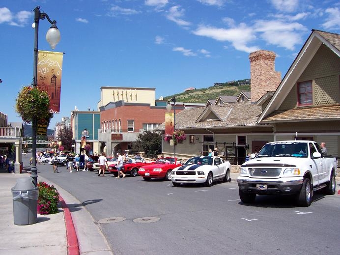 Main-street car show with white Ford F-150, striped Mustang and red classics at the curb