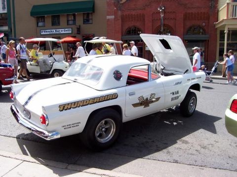 1972 Ford Ranchero - A white Ford Thunderbird is parked on a street with its hood up, displaying racing decals and text.