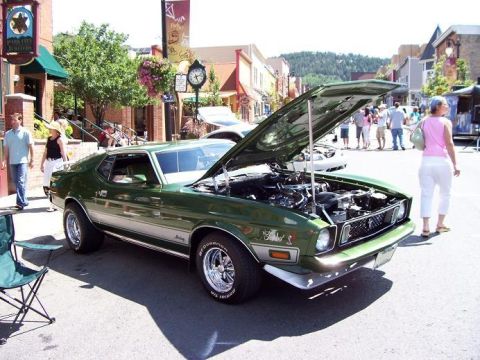 1972 Ford Ranchero - A green 1971 Ford Mustang Mach 1 is displayed with its hood open on a sunny day in a town square.