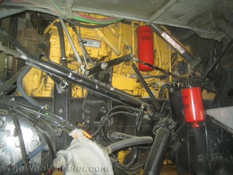 1990 Ford Bronco - yellow diesel engine viewed from underneath, surrounded by red spin-on filters, hoses and steering linkage.