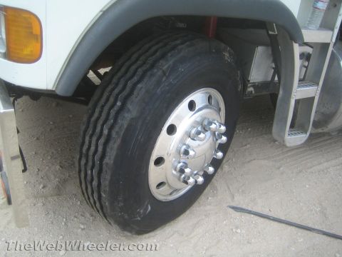 1990 Ford Bronco - Close-up of a white commercial truck's front steer wheel with a polished aluminum rim, chrome lug nut covers, and an amber side-marker ligh…