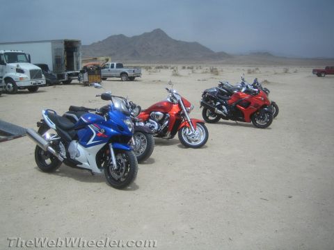1990 Ford Bronco - blue sportbike, red cruiser, black sportbike and red sportbike parked on desert dirt with a transport truck and trailer in the background.