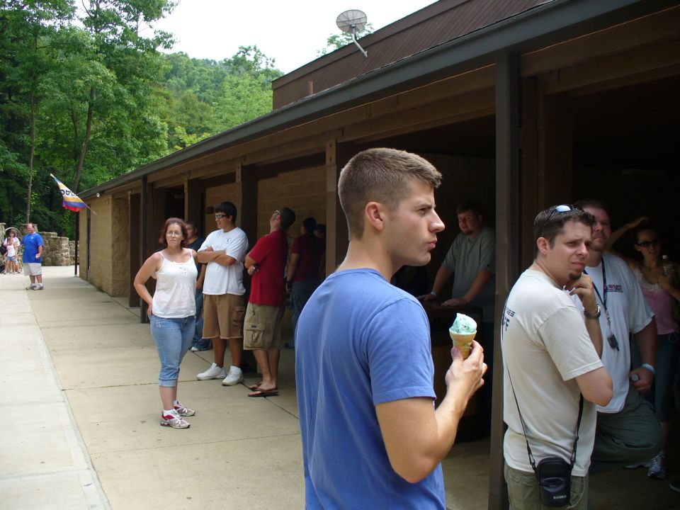 Guy in blue shirt holding ice cream, people standing around a building