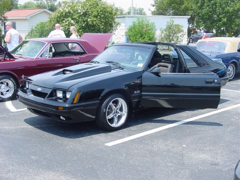 1986 Ford Mustang - A black Ford Mustang hatchback is parked at an outdoor event with other vehicles visible.