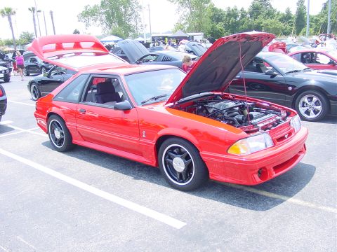 1986 Ford Mustang - A red 1986 Ford Mustang coupe is displayed with its hood and trunk open at an outdoor car show.