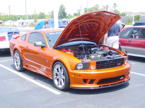 1986 Ford Mustang - Orange Ford Mustang with hood open at an outdoor car show.