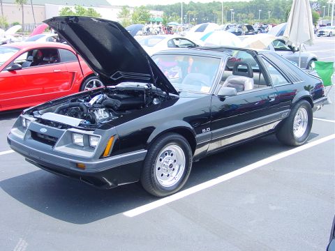 1986 Ford Mustang - This black 1986 Ford Mustang GT, identified by its 5.0 badge and body style, is displayed with its hood open at an outdoor car show.