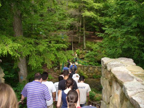 1991 Ford Probe - A group of people ascend a path surrounded by lush green trees and stone structures.