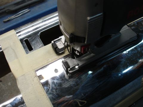 1996 Ford Bronco - A jigsaw is used to cut into a shiny chrome bumper, with masking tape marking the area.