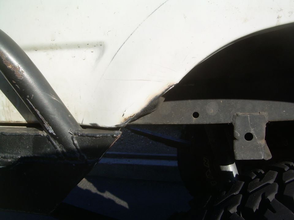 close-up of white vehicle's rear fender well, showing rust and aftermarket roll cage attachment