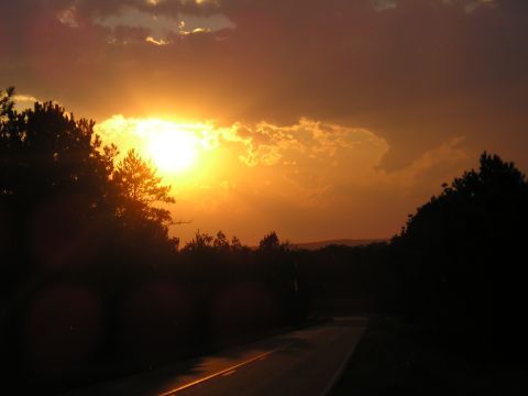 1989 Ford Bronco - A road stretches into the distance under a dramatic sunset sky with silhouetted trees.