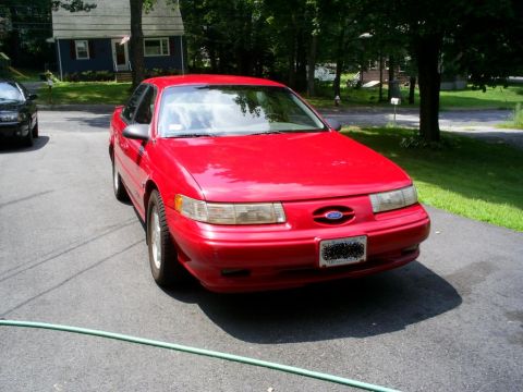 1995 Ford Taurus - A red 1995 Ford Taurus is parked in a driveway on a sunny day.