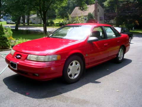 1995 Ford Taurus - A red 1995 Ford Taurus sedan is parked on an asphalt driveway on a sunny day.