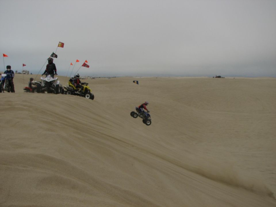 Riders on ATVs at sand dunes with whip flags under gray sky