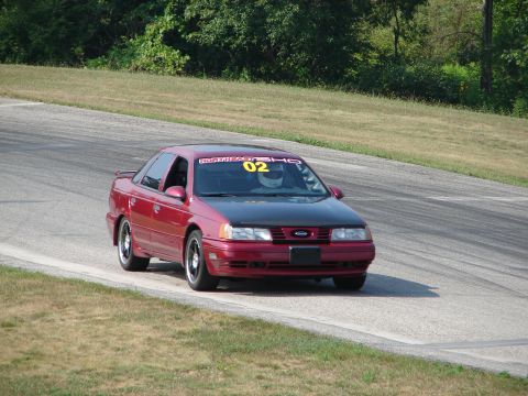 1993 Ford Taurus - Red 1993 Ford Taurus SHO racing on a track with a driver wearing a helmet.