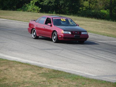 1993 Ford Taurus - A red 1993 Ford Taurus with a black hood is seen on a race track during a track day event.