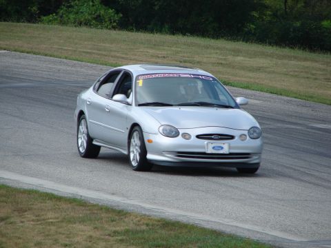 1993 Ford Taurus - A silver sedan navigates a turn on a road course, displaying a banner across its windshield.