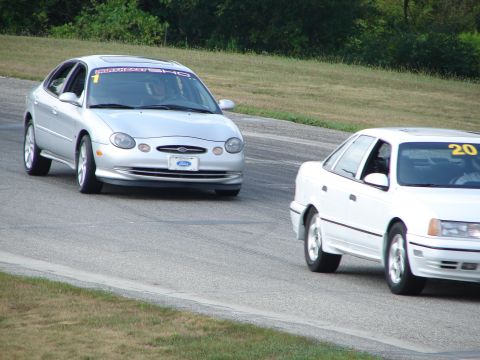 1993 Ford Taurus - A silver 1996 Ford Taurus with a "NORTHEAST SHO" banner races on a track alongside another car.